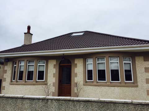 House with brown roof and white gutters. Velux window in roof